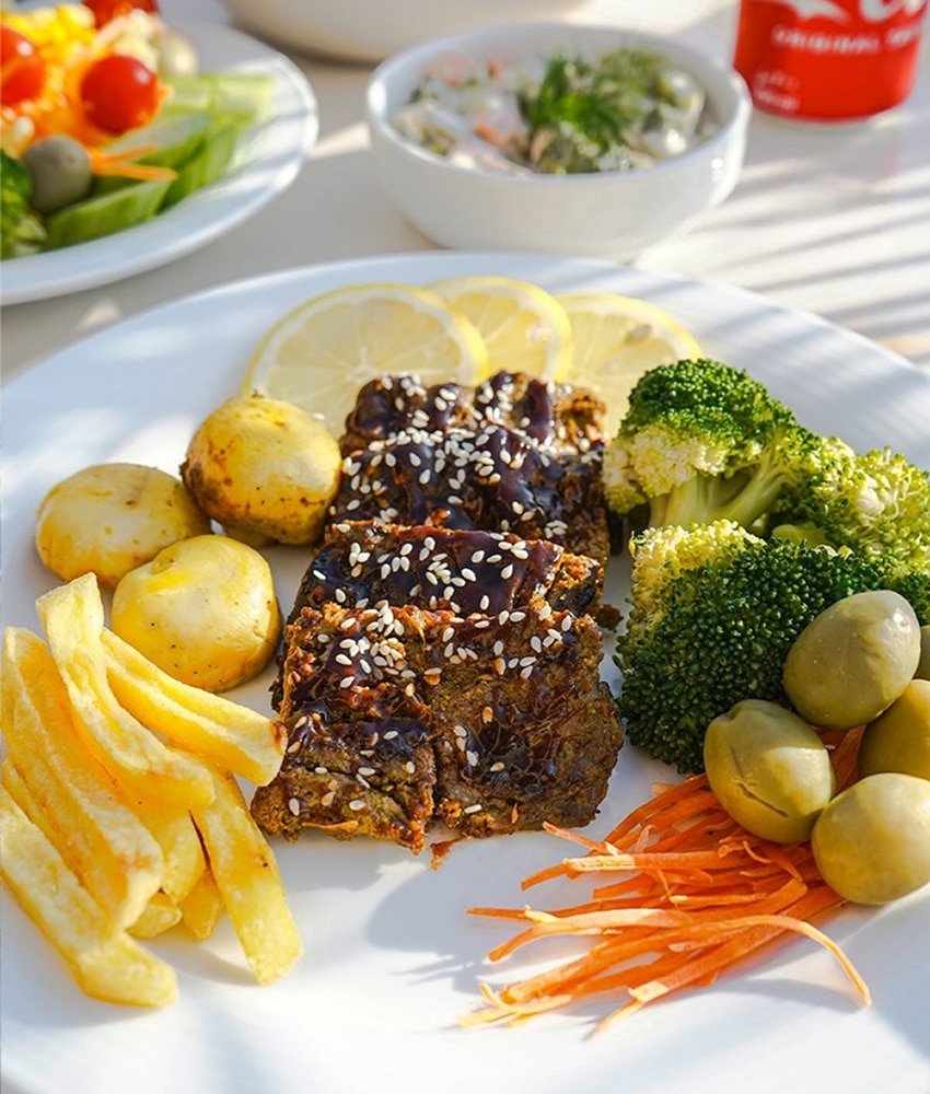 Grilled meat slices topped with sauce and sesame seeds served with potatoes, broccoli, olives, and vegetables at Danial Star Restaurant