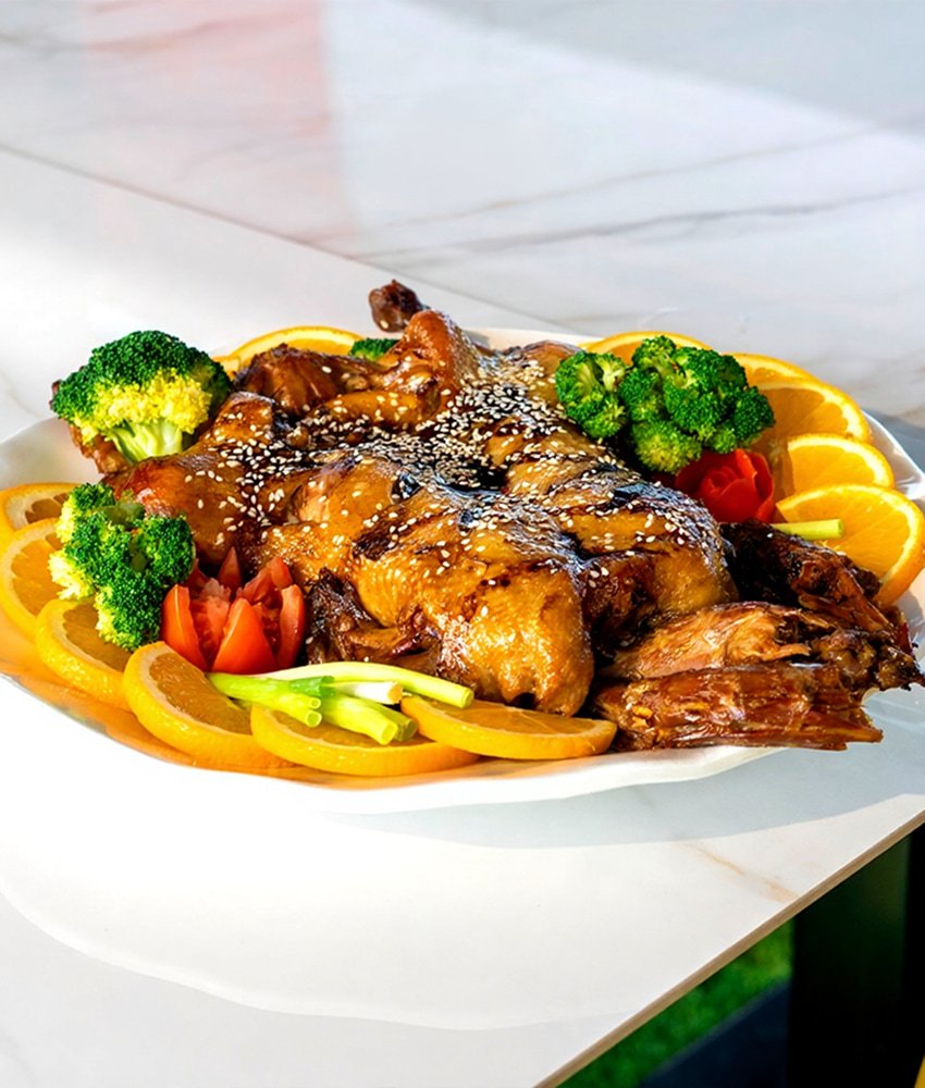 Whole roasted chicken glazed with sauce and sesame seeds, served with broccoli, oranges, and vegetables at Danial Star Restaurant