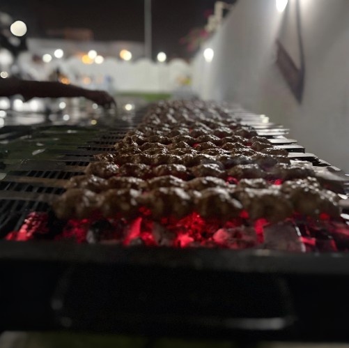 Rows of sizzling kebabs grilling over hot charcoal at an outdoor barbecue setup at night